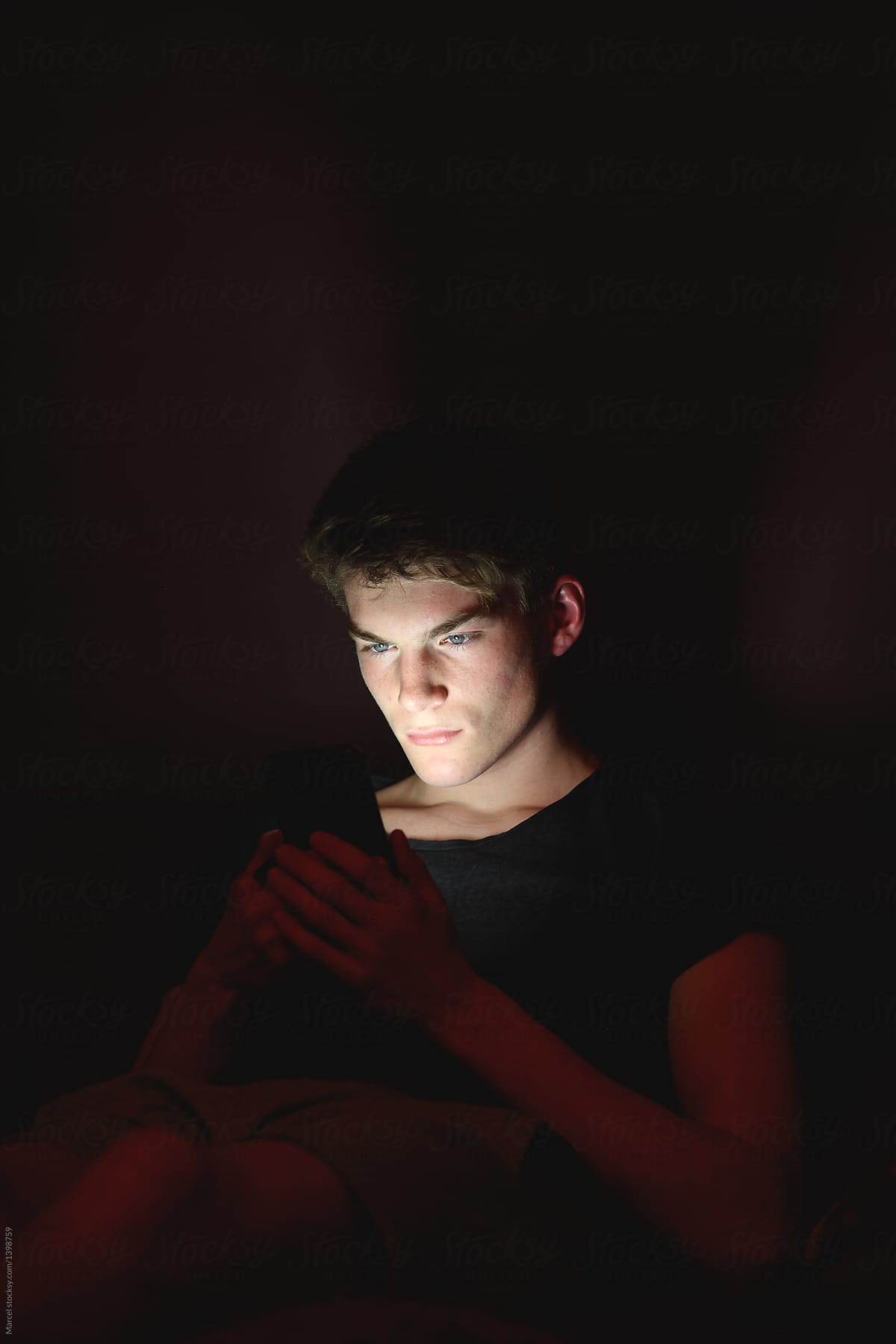 Young man resting on a couch using his phone in the dark