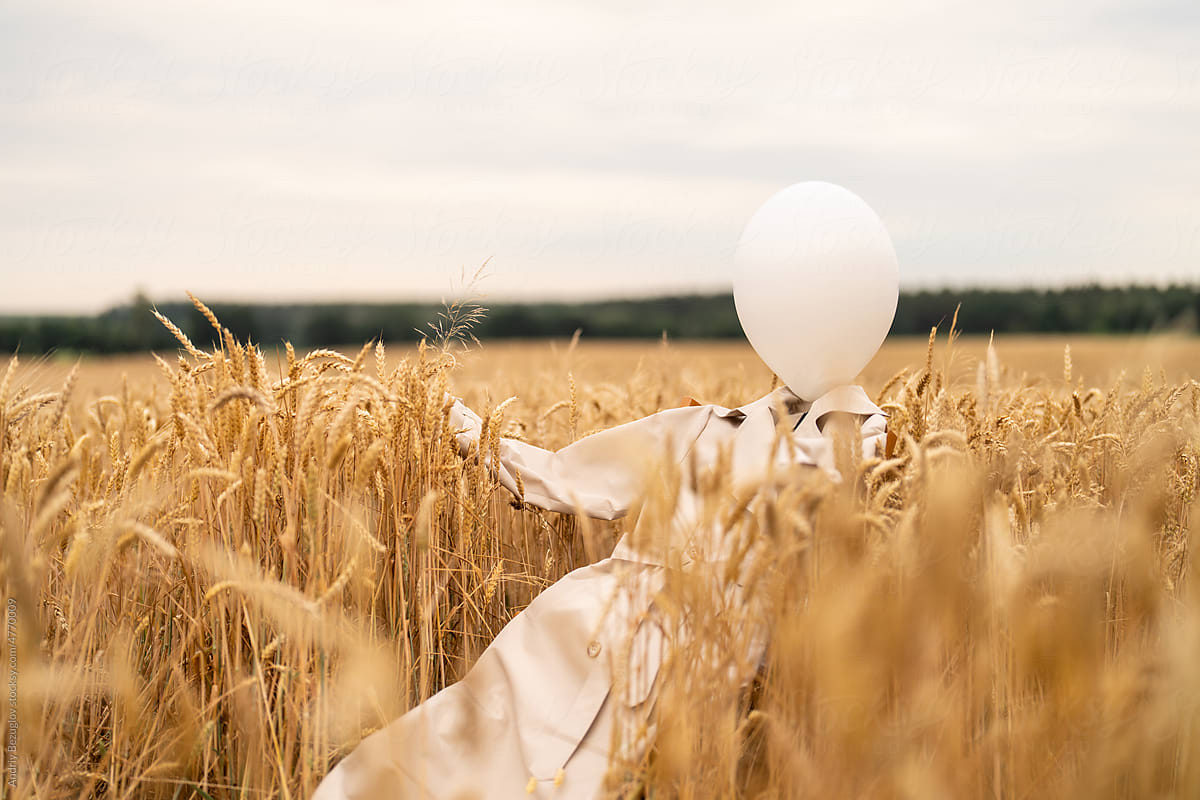 Beige trench coat laying around wheat field with white balloon inside