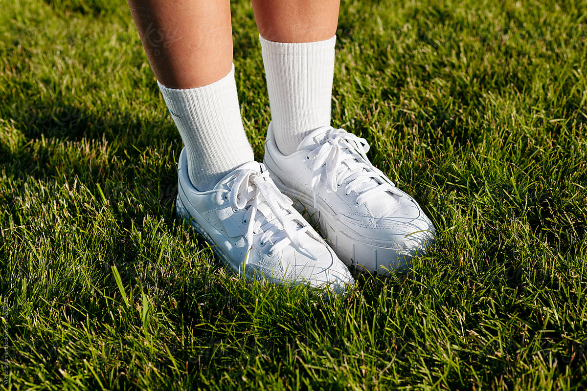 Legs of person in sneakers on green fresh grass of football stadium
