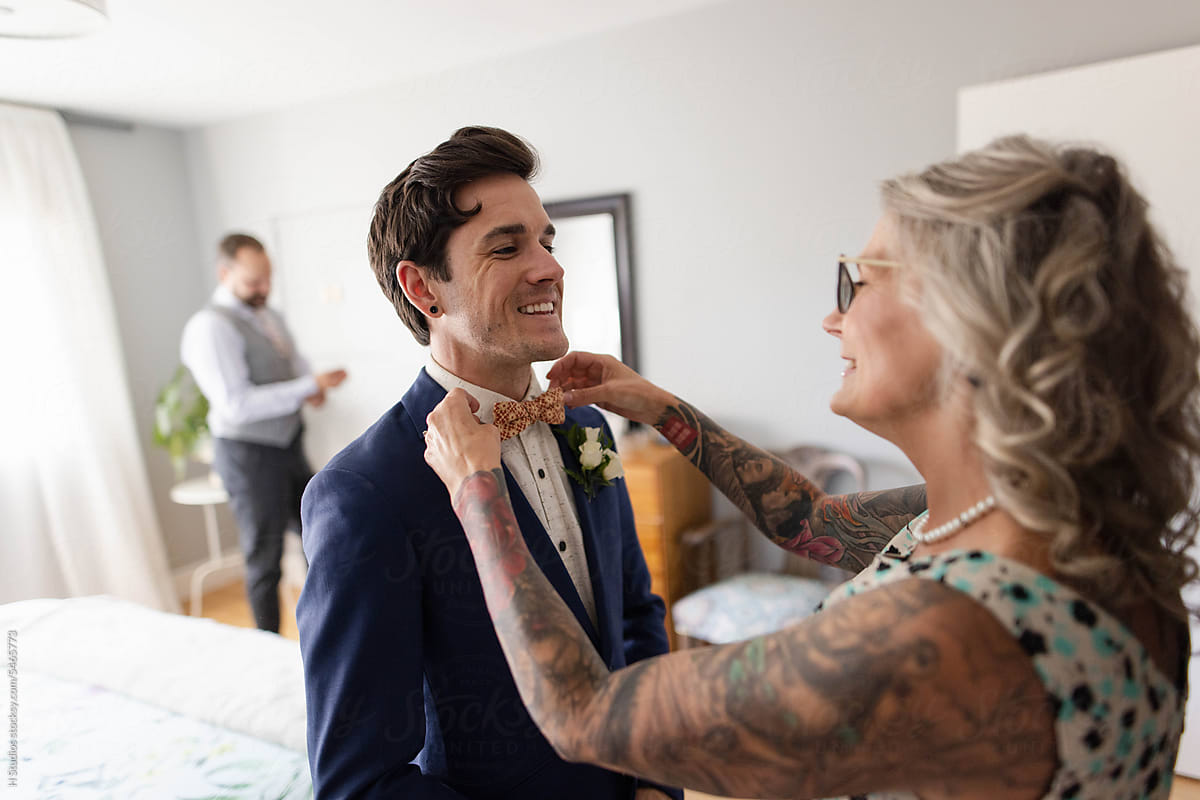 Happy mother helping gay son with bowtie on his wedding day