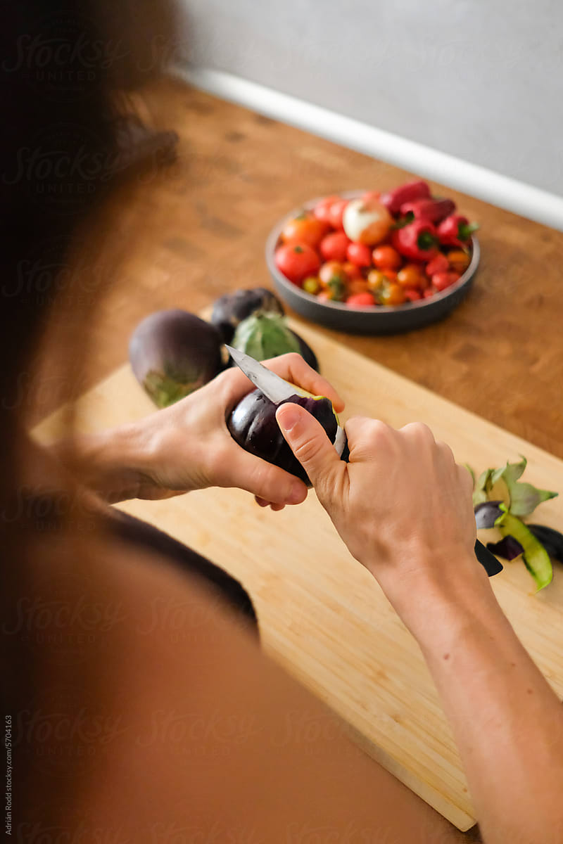 Close up of a woman using a kitchen knife to slice fresh eggplants