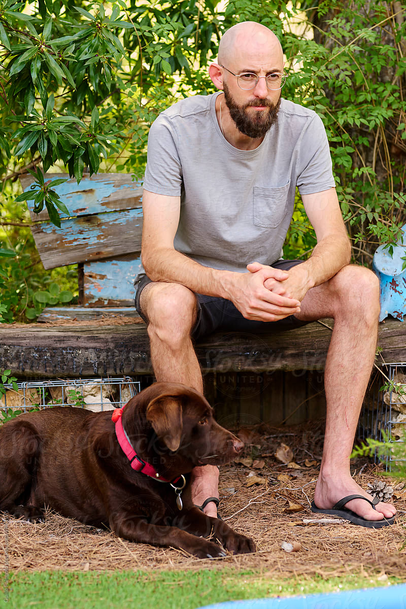 Pensive man with Labrador in garden.