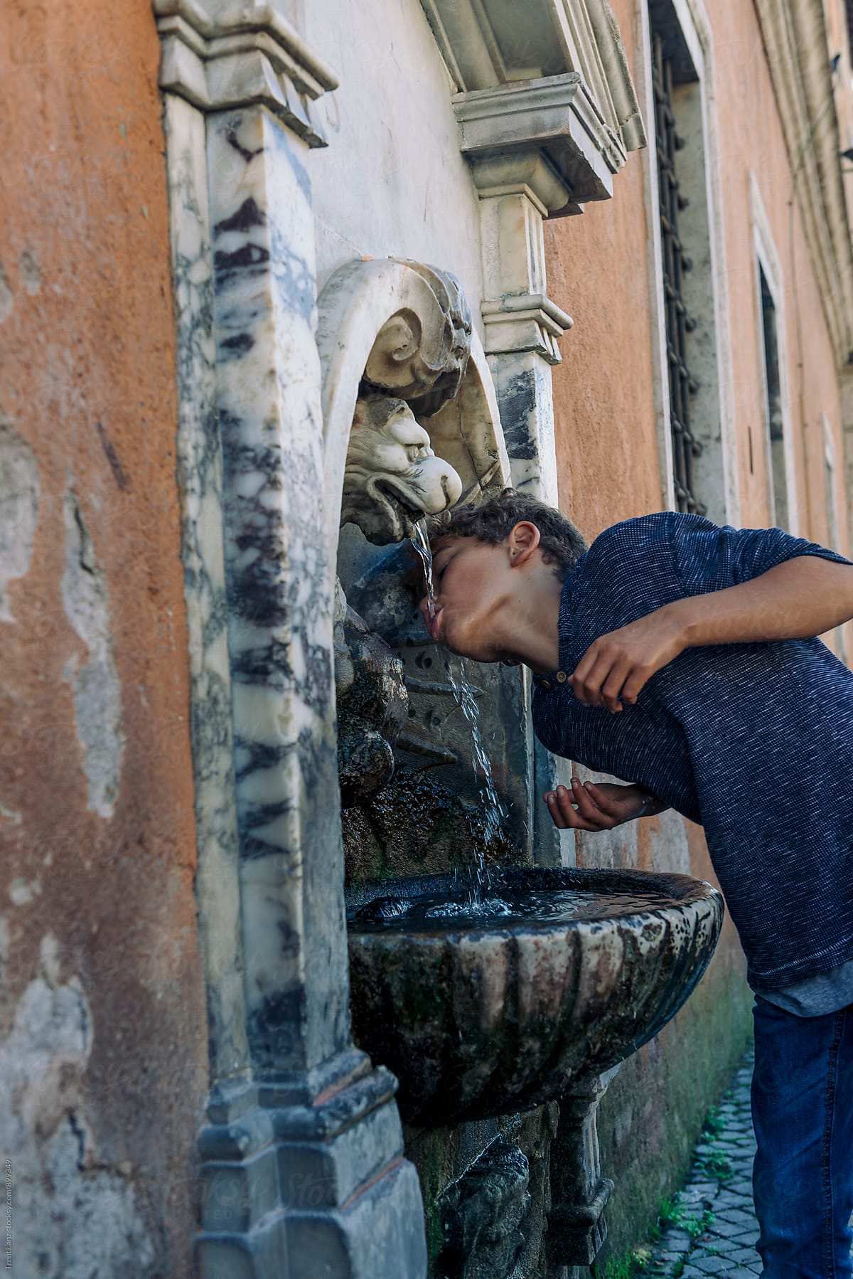 Boy drinking water from marble fountain on street in Rome