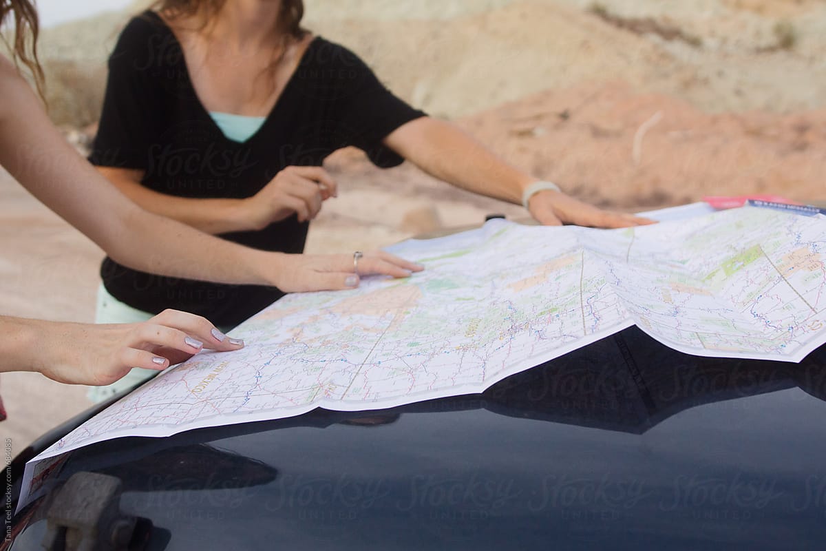 map spread on hood of vehicle while women plan direction