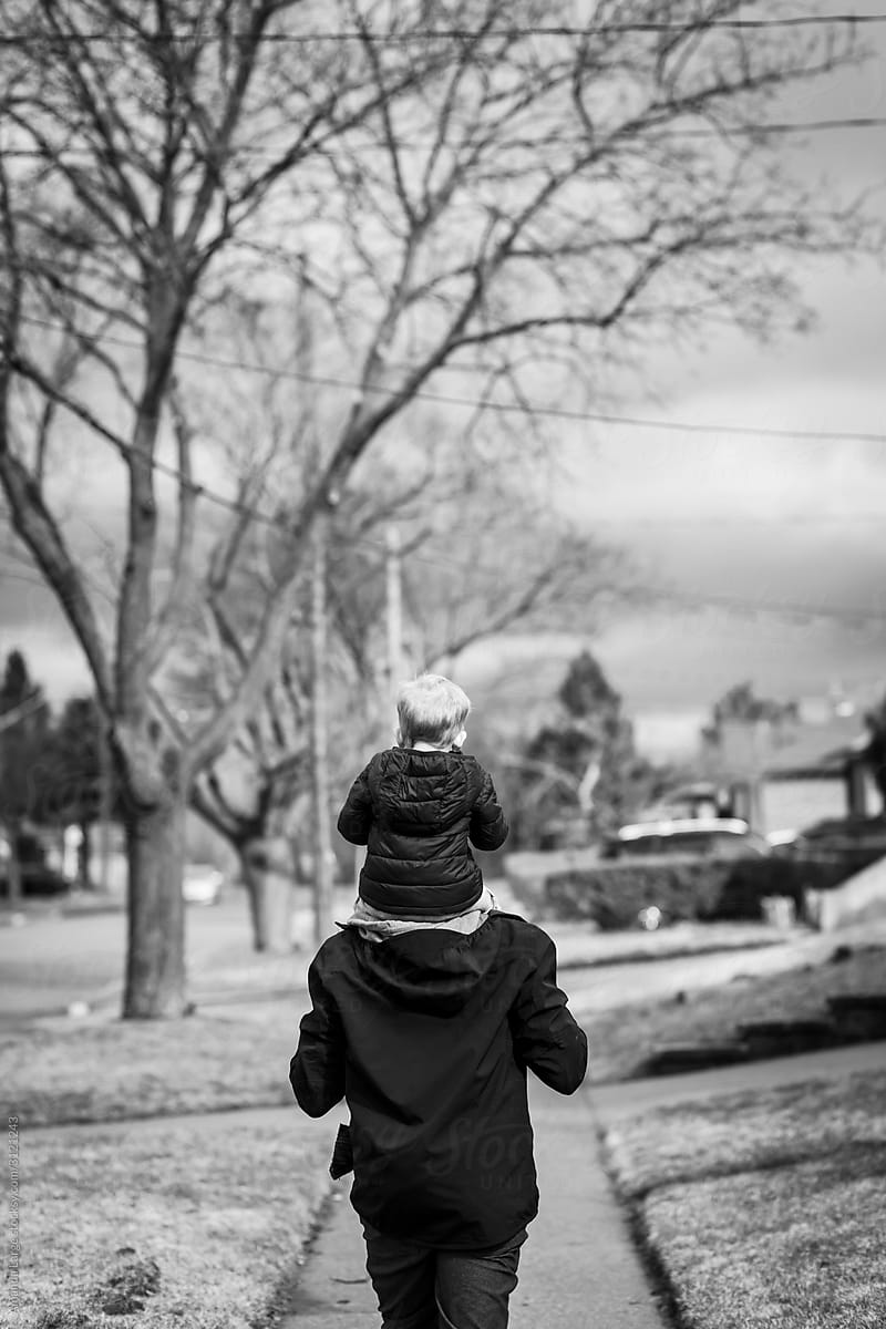 A toddler boy is out for a walk with his father in a suburban neighbourhood.