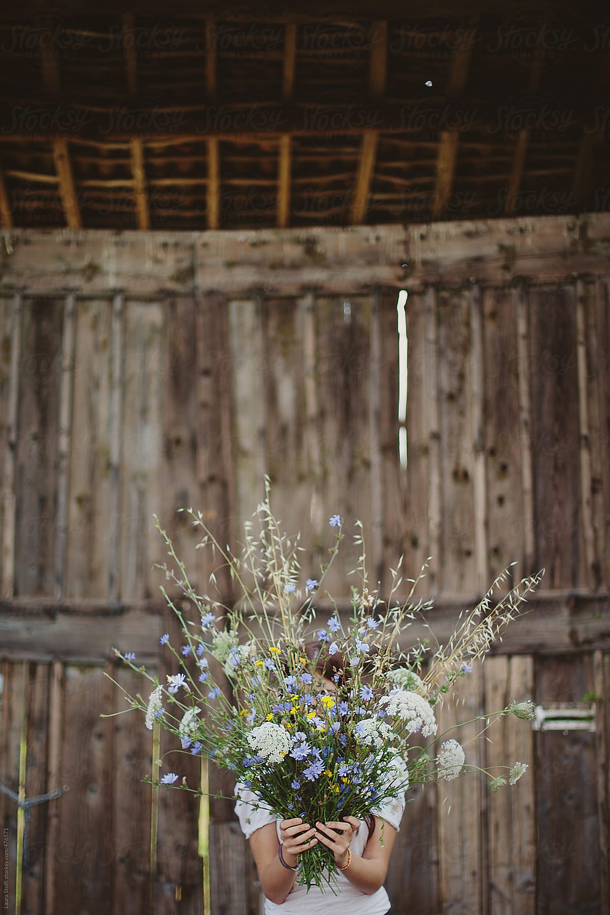 Woman hides her face behind flowers bouquet in front of old wooden door
