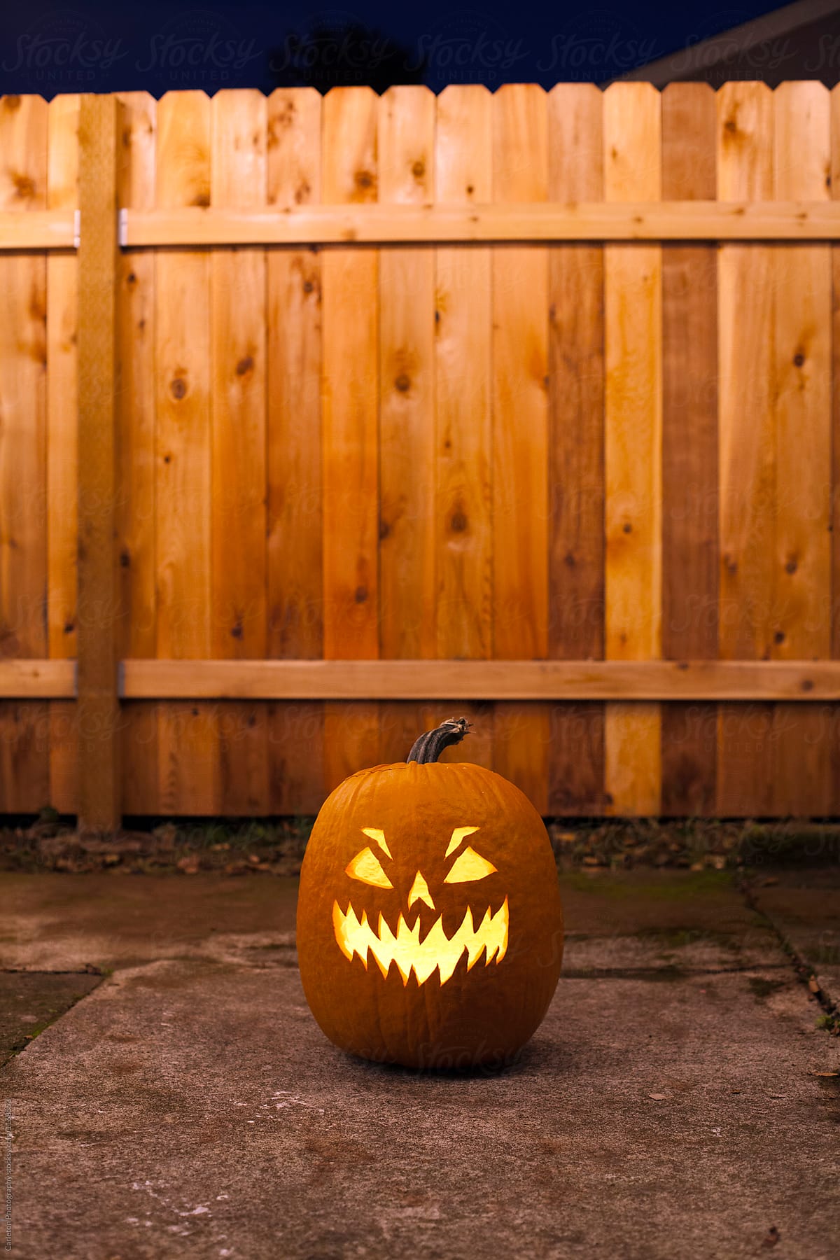 Jack-o-lantern lit up in front of a fence