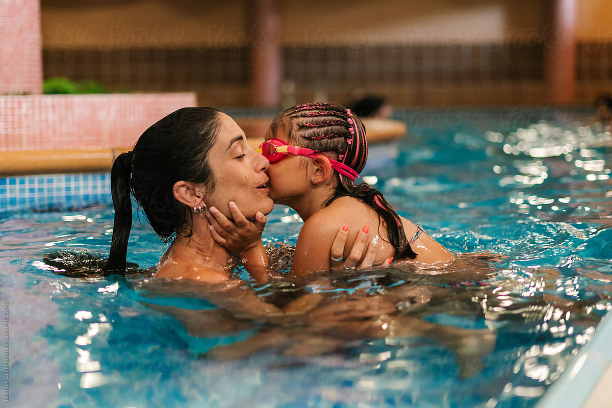 Cute kid kissing mom on cheek in swimming pool