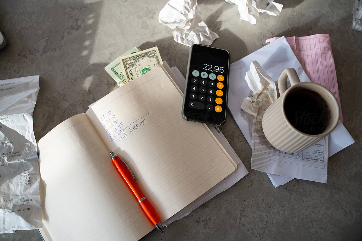 Messy workspace: phone calculator, notebook, cash money, receipts