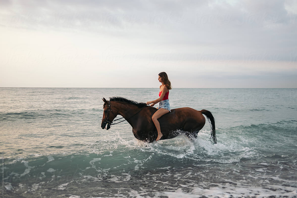 Young woman riding a horse into the sea