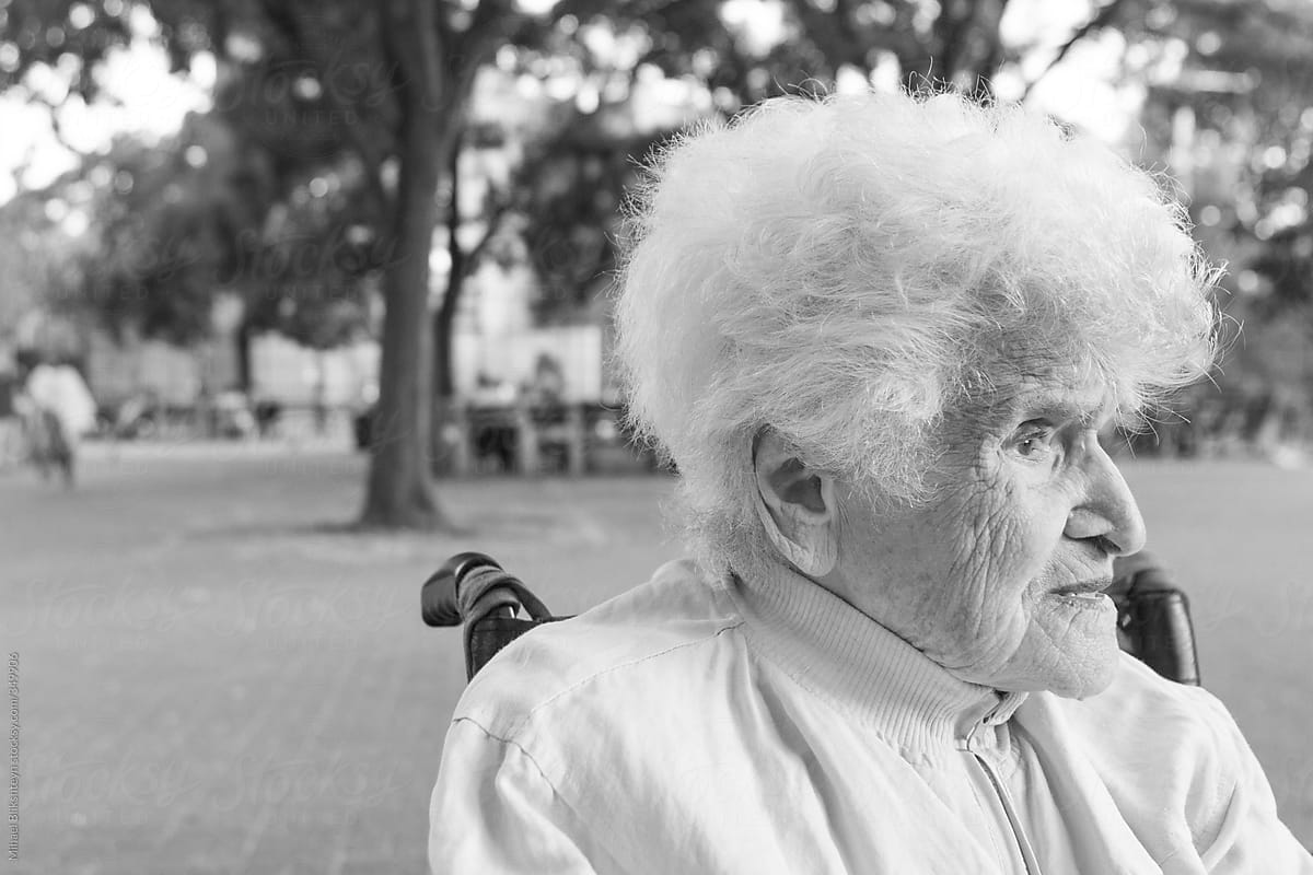 Black-and-white photo of an elderly woman in wheelchair at the park looking into the distance