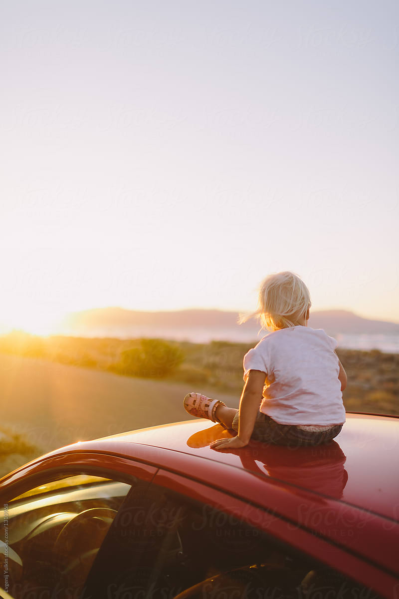Baby girl sitting on car top at sunset