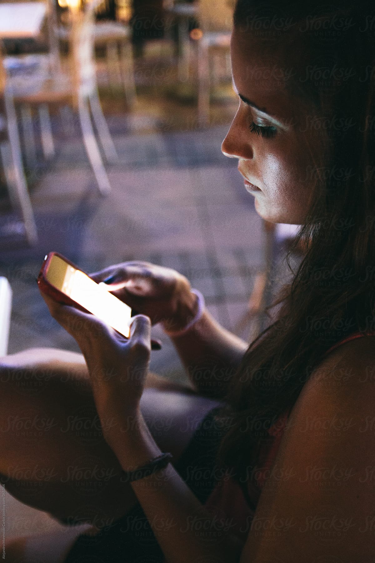 Young beautiful woman texting with her mobile phone at night on a restaurant terrace