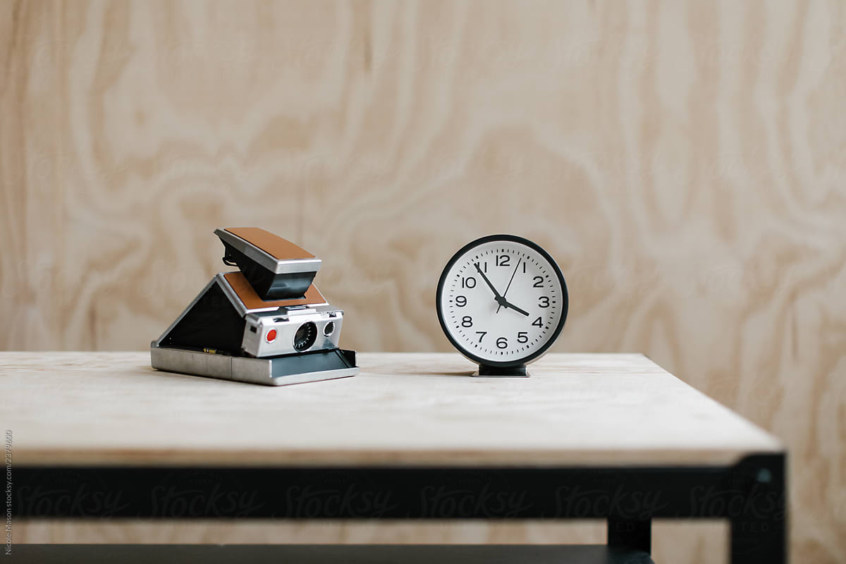 vintage instant camera and analog clock on a table with plywood background