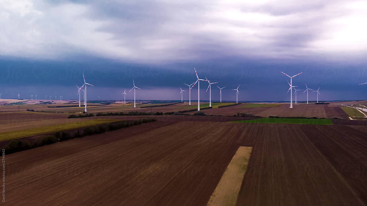 Windmills in cultivated agricultural fields under cloudy sky