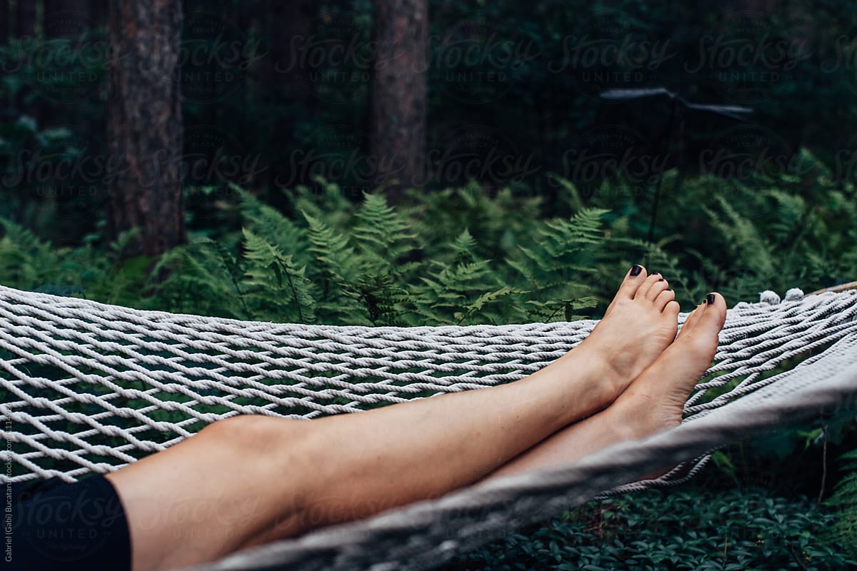 Legs of a woman lounging on a hammock in a forest