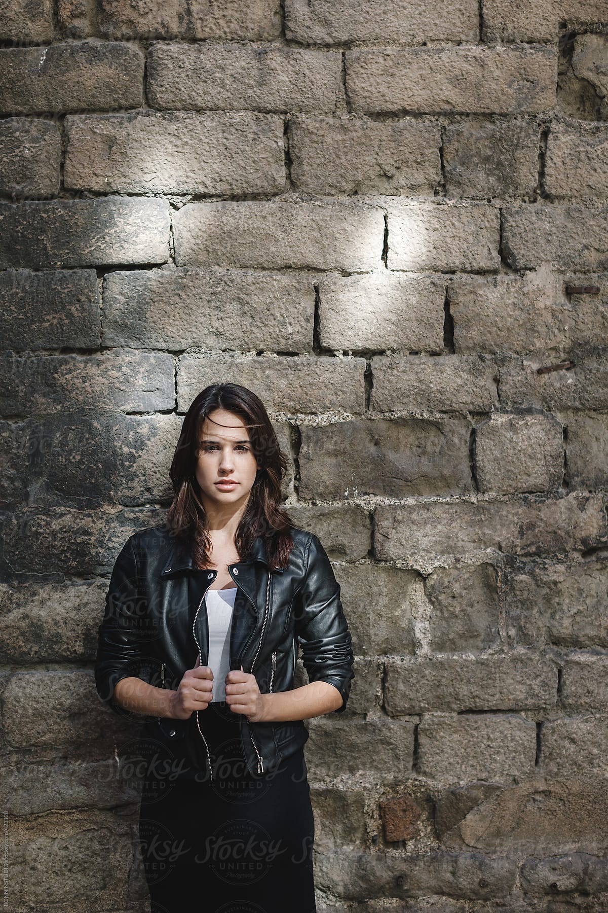 Portrait of young modern woman wearing leather jacket in front old stone wall.