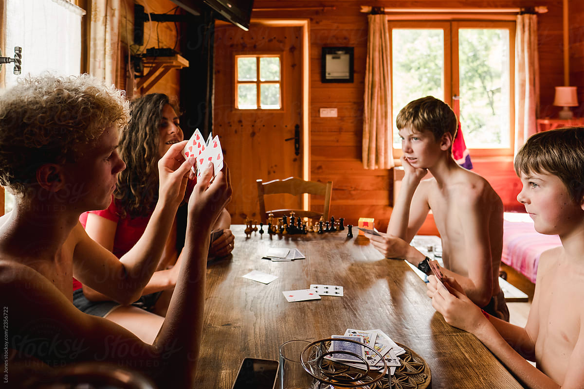 four kids playing a game of cards in the summer in a chalet