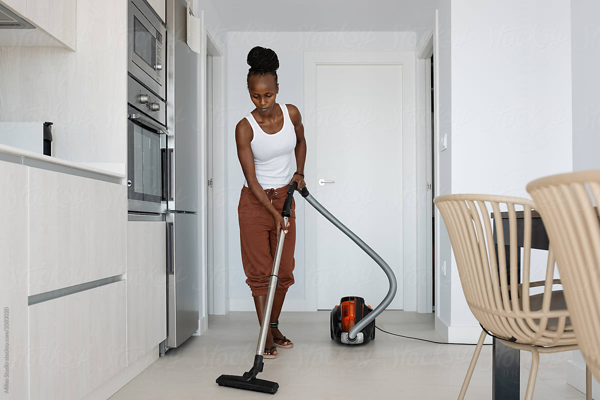 Black housekeeper cleaning floor in light kitchen