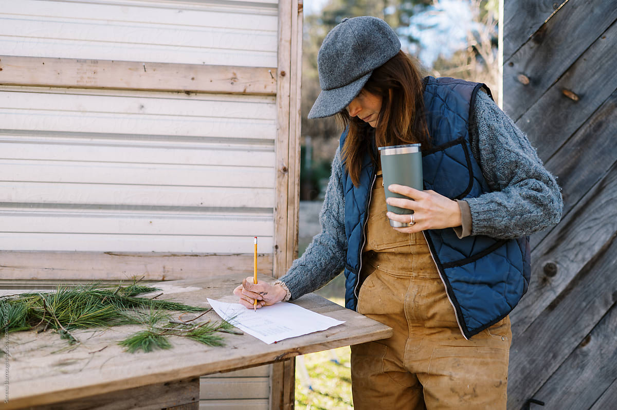 female farm worker with coffee in hand checking off orders on chart