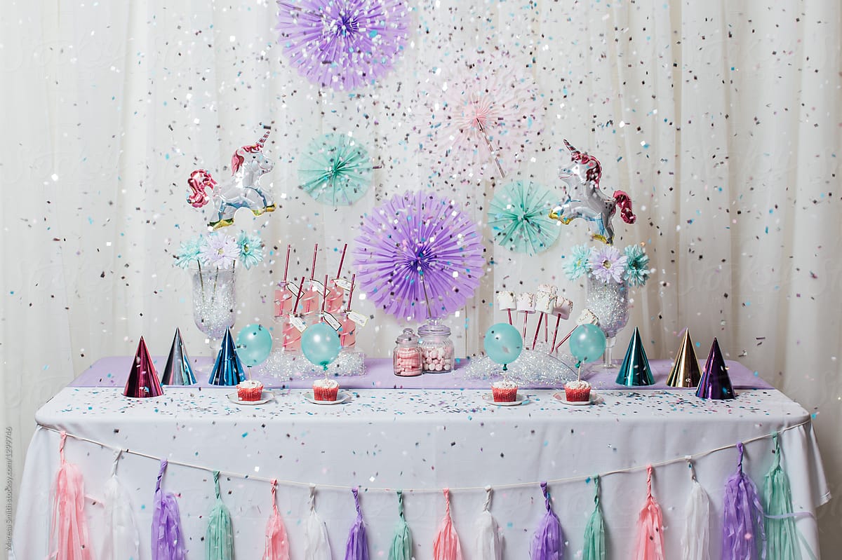 Confetti exploding over a party table, decorated in pastel colours with unicorns, party hats and tassels