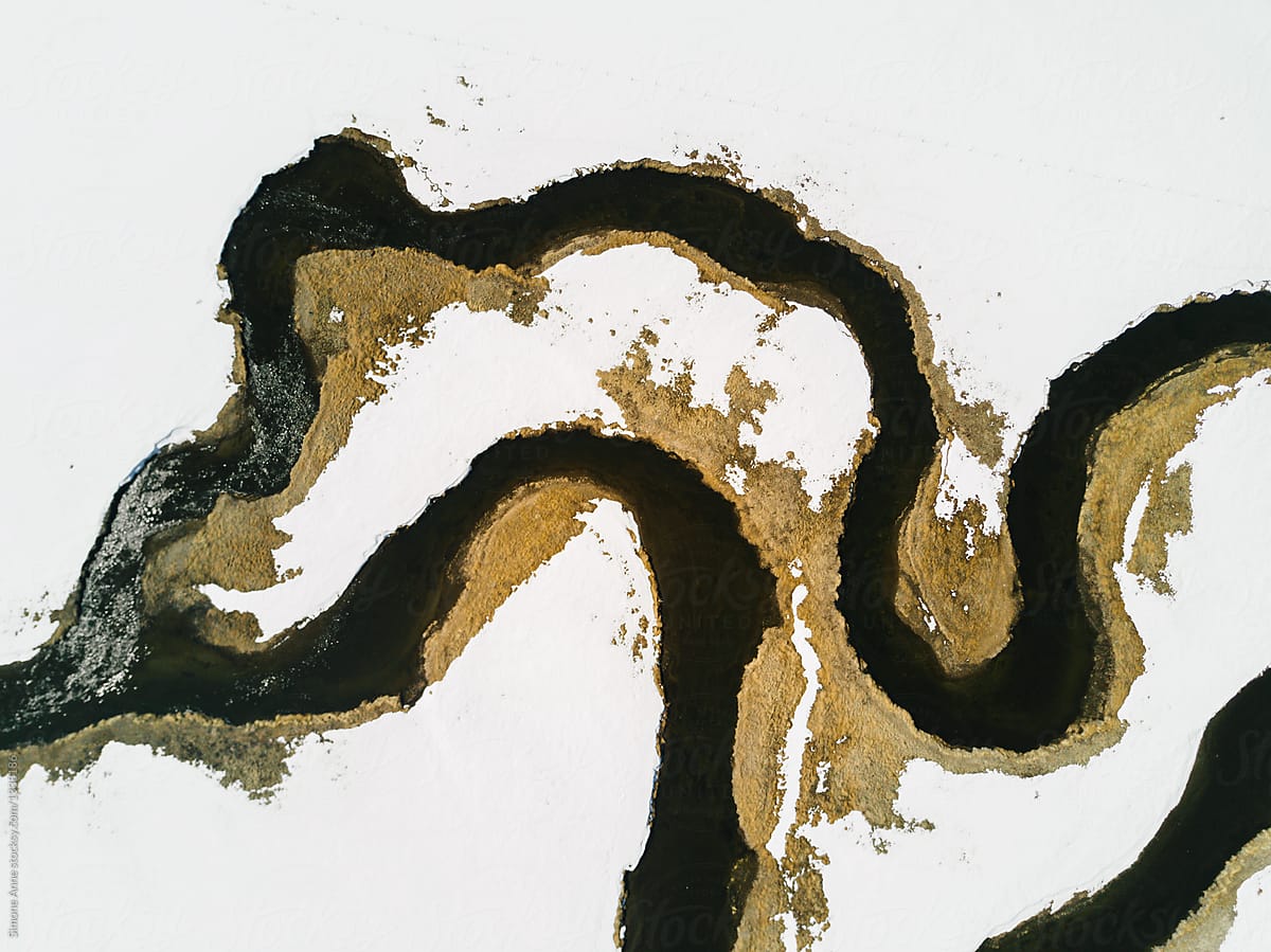 View of a winding navy blue river through a white snowy landscape in California, aerial view
