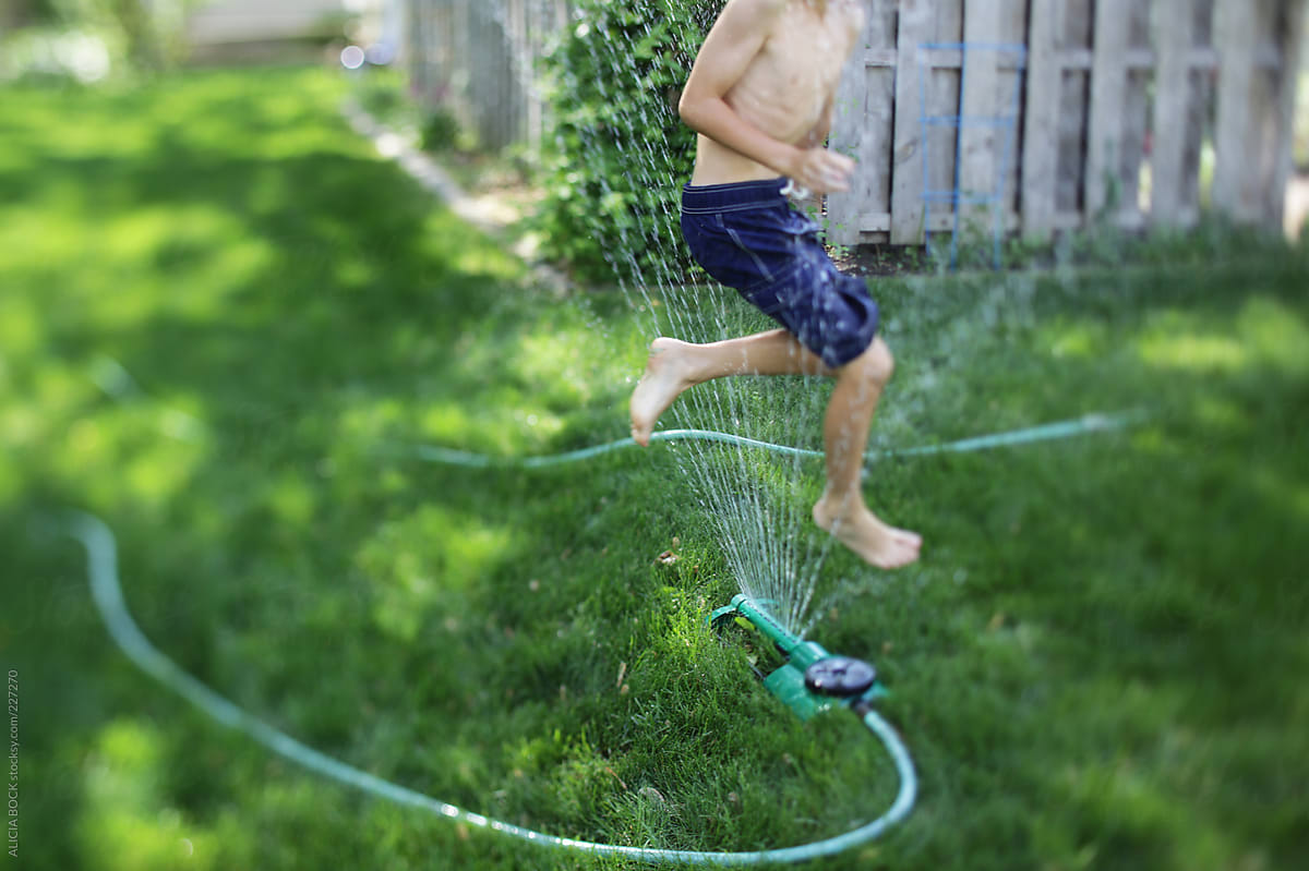 Boy Playing In a Sprinkler In a Green Backyard