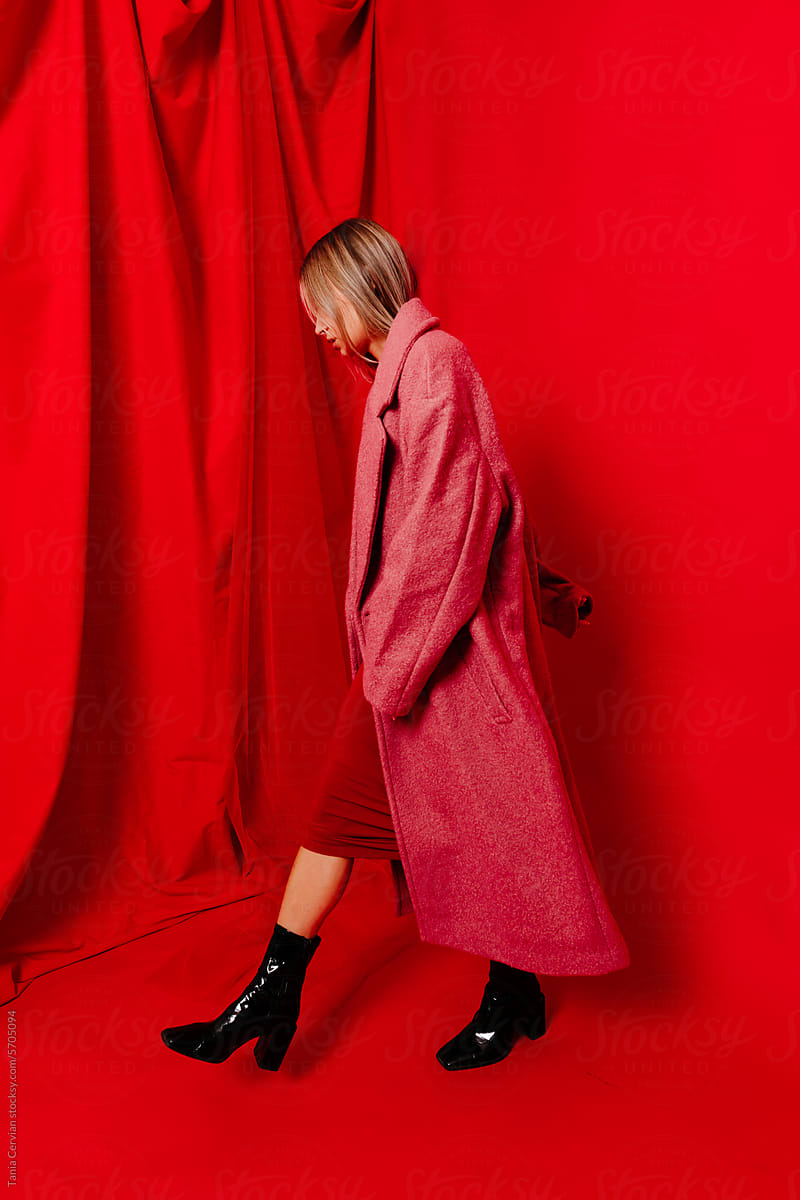 Female model in trendy coat walking over red background