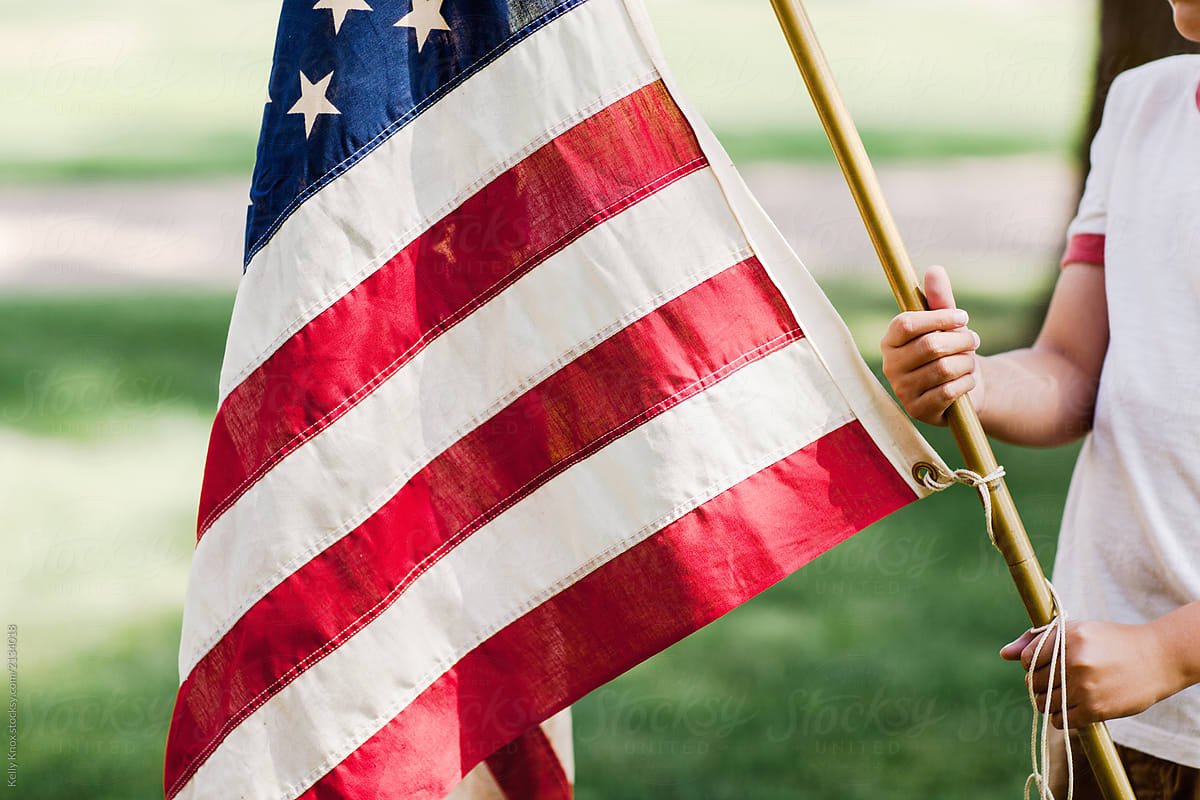 young boy holding an American flag outdoors in the summer