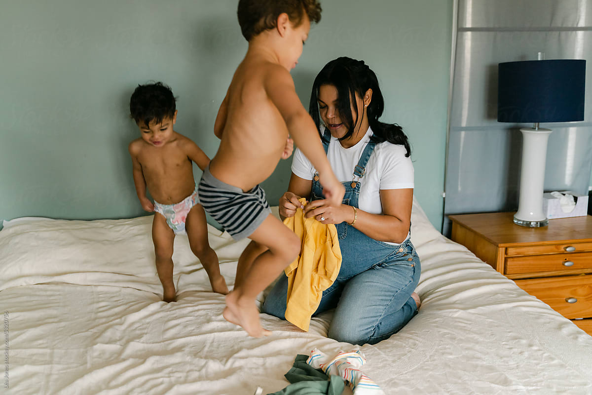 pregnant mother dressing her toddlers on bed, little boys jumping