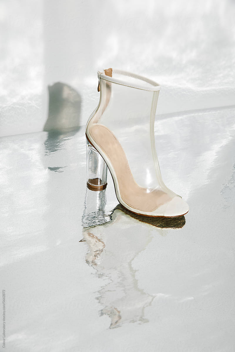 Transparent plastic high heel laying on shiny metal silver background