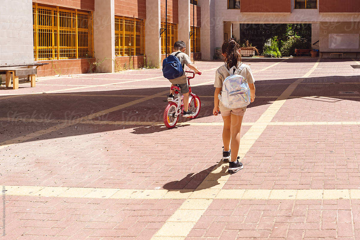 Sunny School Journey. Girl Walks, Boy Rides Bike to School Yard.