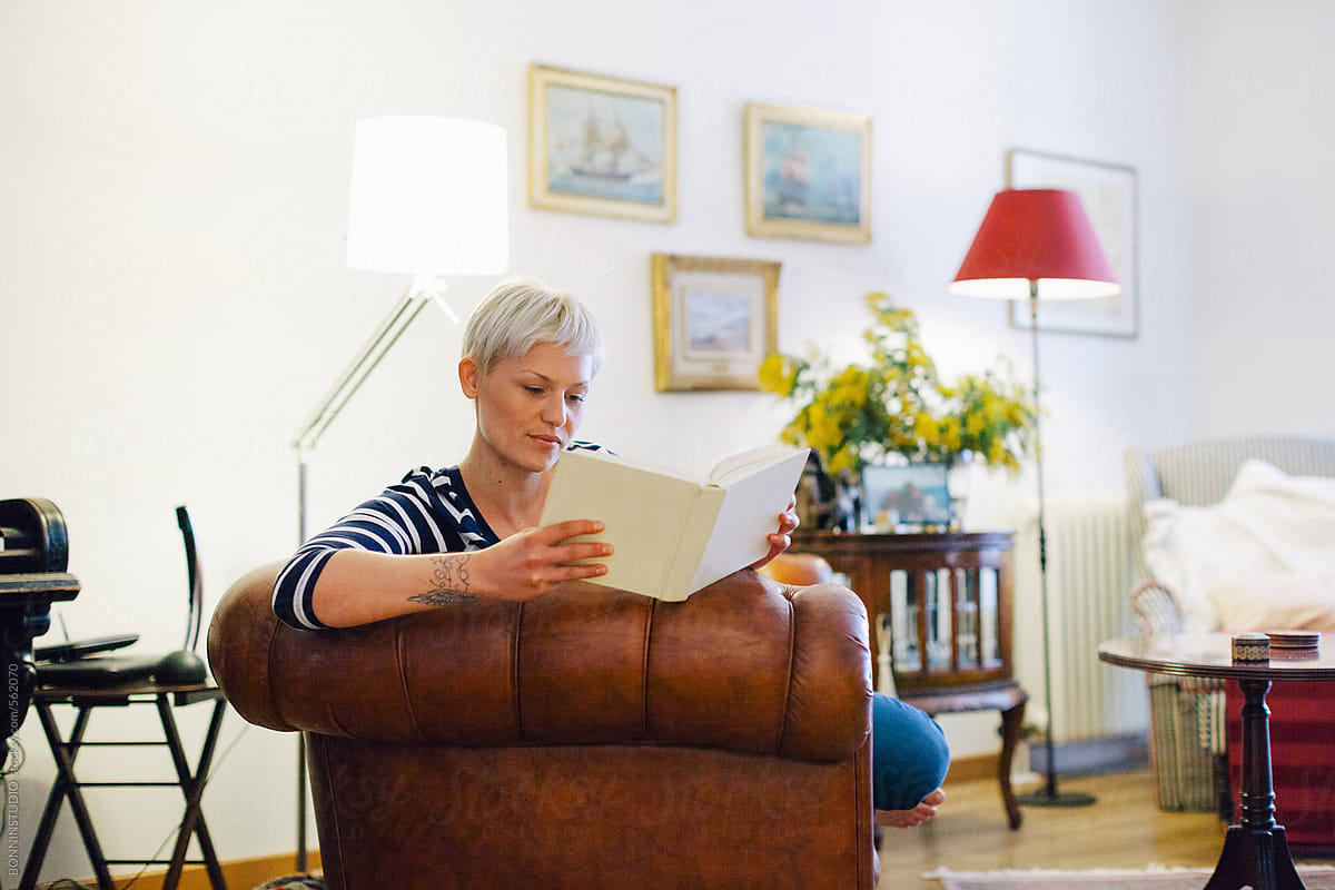 Beautiful Blonde Woman Reading A Book On The Couch At Home Del Colaborador De Stocksy