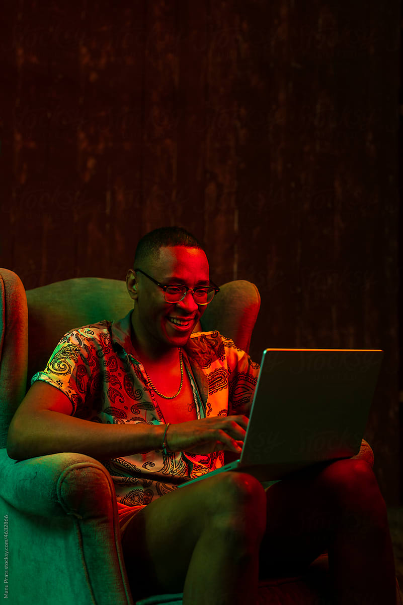 Brown skinned man using laptop at home with neon lights
