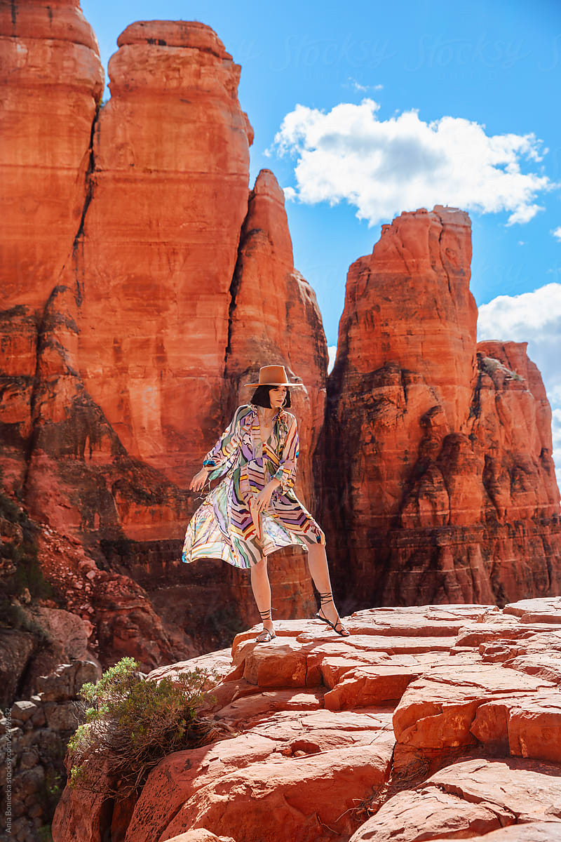 Stylish Cowgirl in dress stands in front of rock formation.