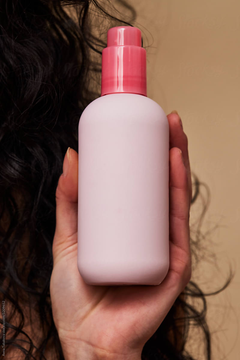Woman\'s hand holding pink skincare bottle