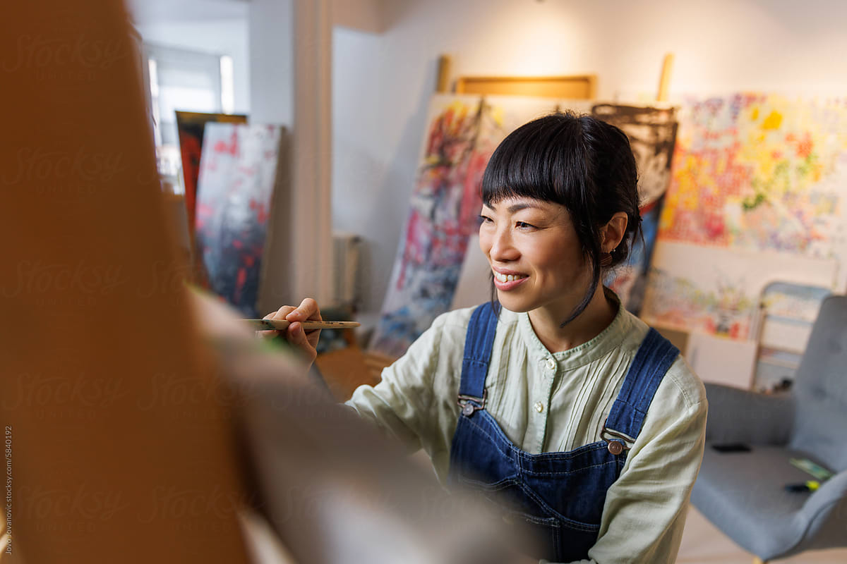 Closeup of smiling artist painting on canvas in studio