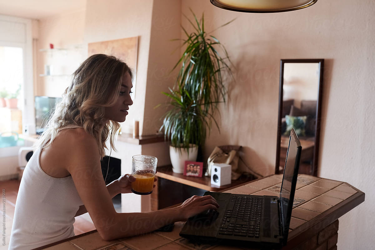 Woman with laptop and orange juice in kitchen