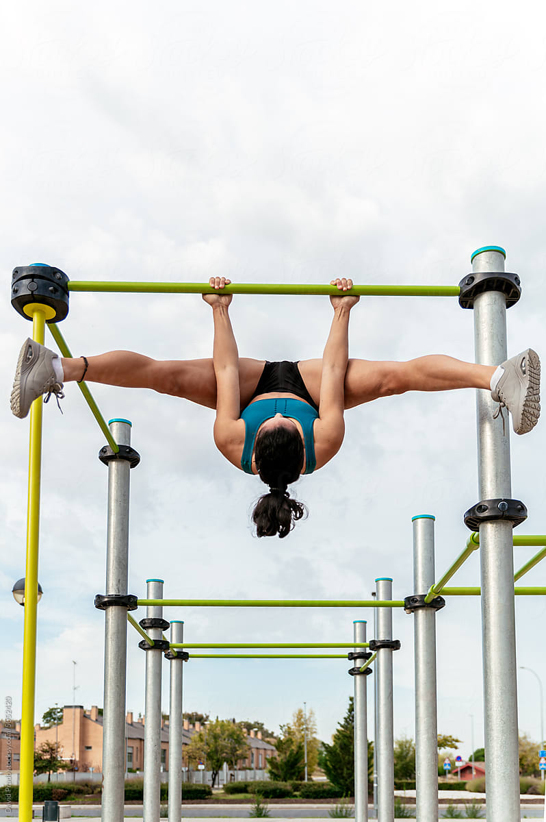Motivated sportswoman hanging on bar and doing split
