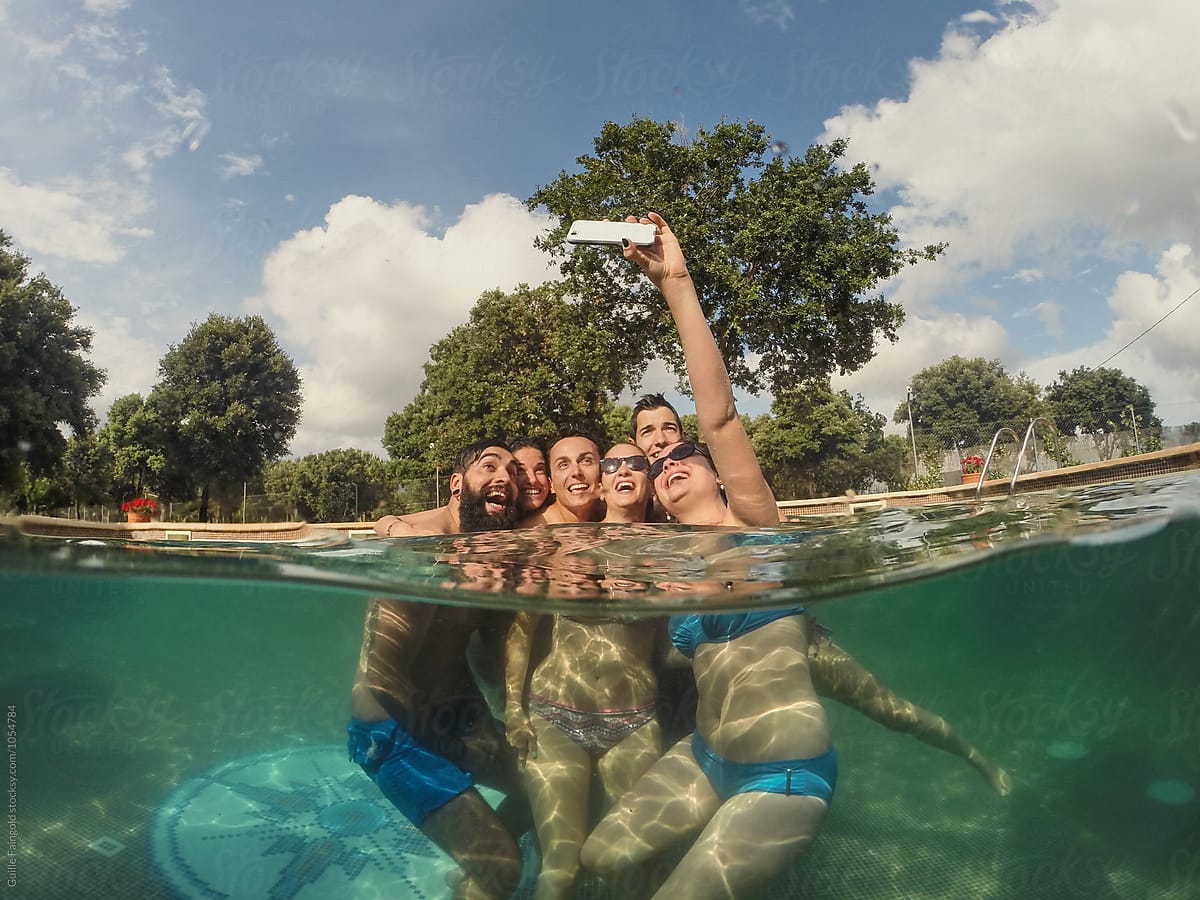 cheerful friends taking selfie using phone in pool