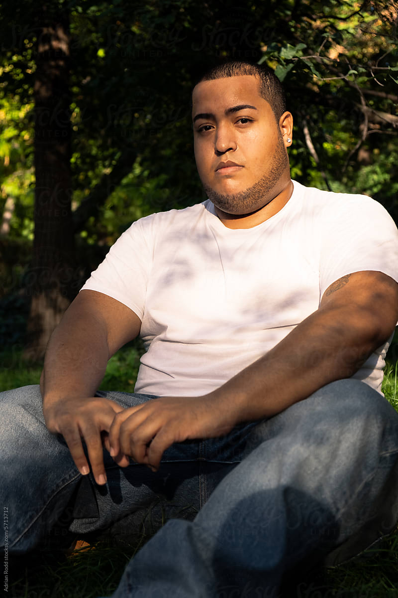 Black Plus-Size guy sitting on the grass looking into the camera.