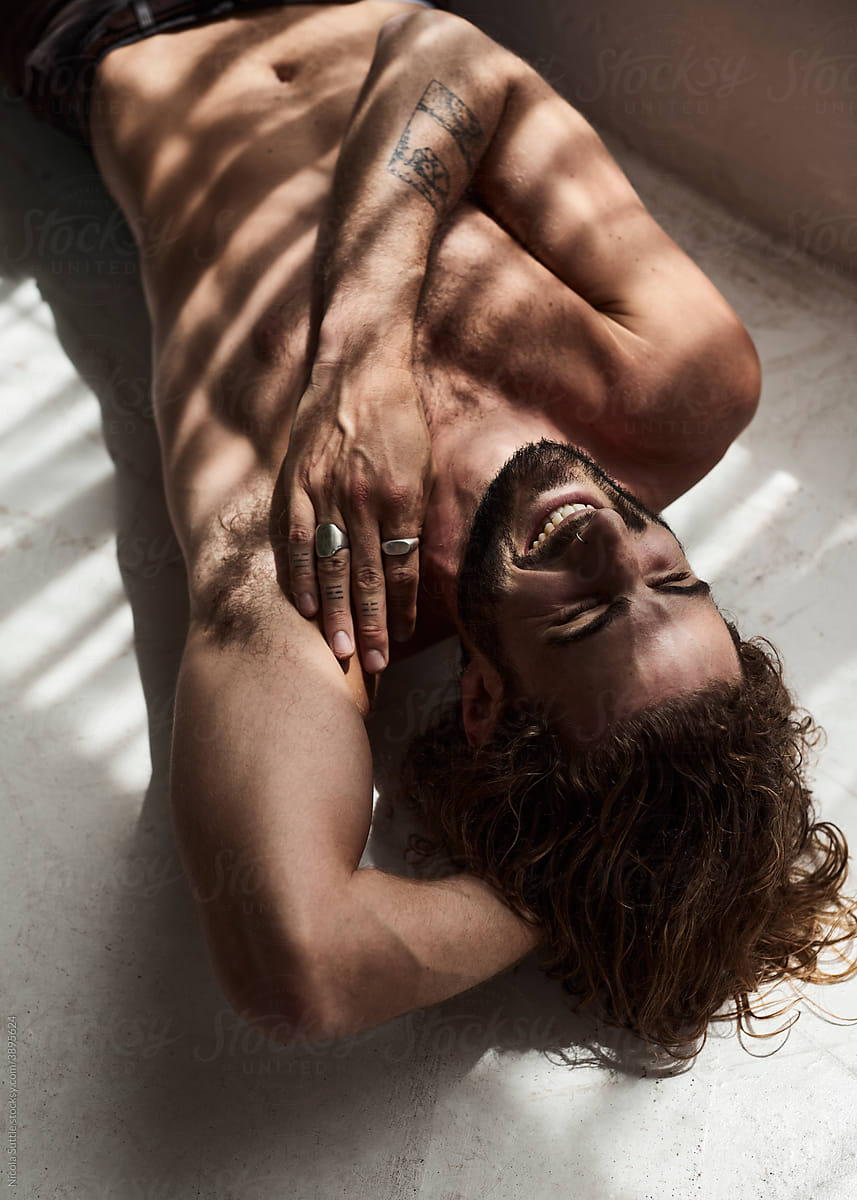 A sexy young man laughing while shirtless on the floor