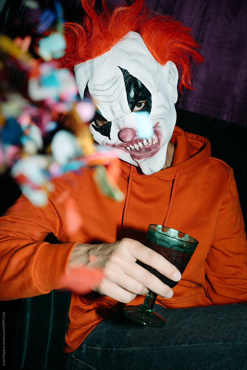 man wearing a mad clown mask holds a green glass in a party