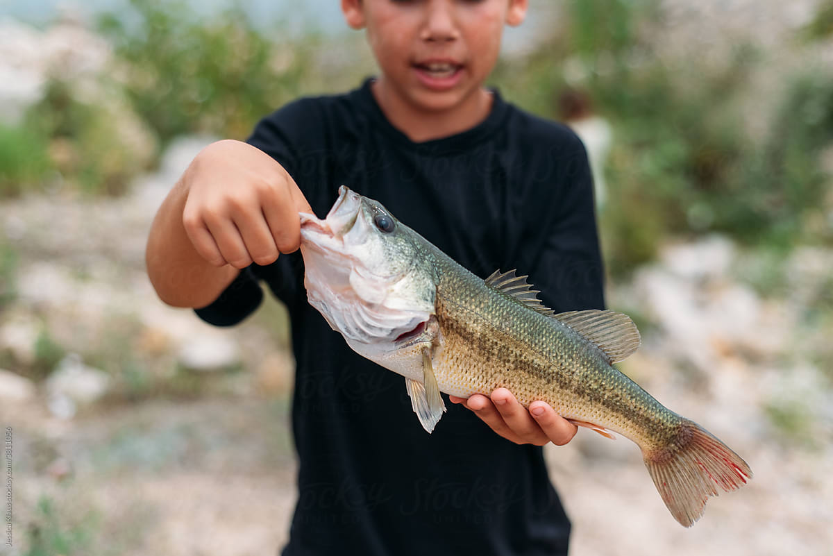 Child holding up large fish by its mouth.