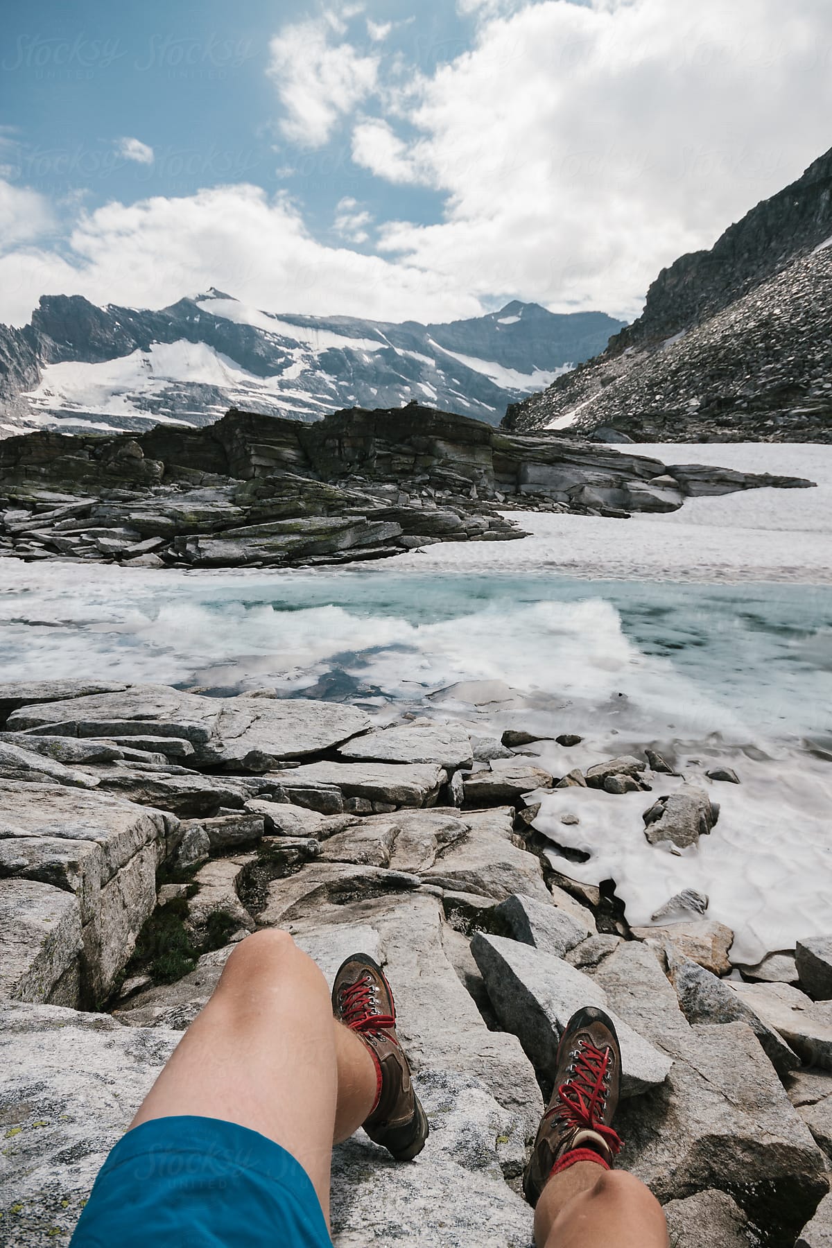 male feet of a hiker in high alpine terrain in front of a small glacier lake