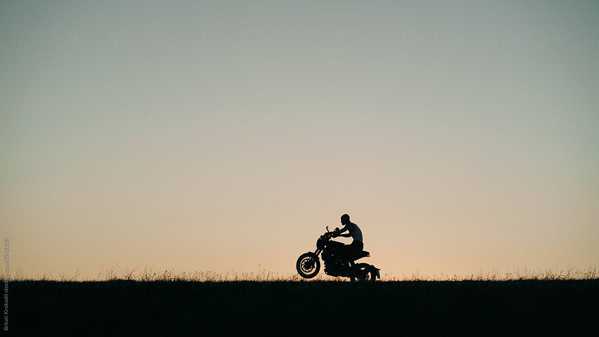 Silhouette Of A Man Riding Motorcycle On One Wheel