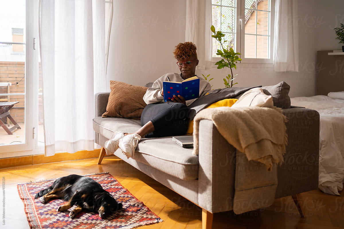 Black Woman Taking Notes On A Book Next To Her Dog At Home.