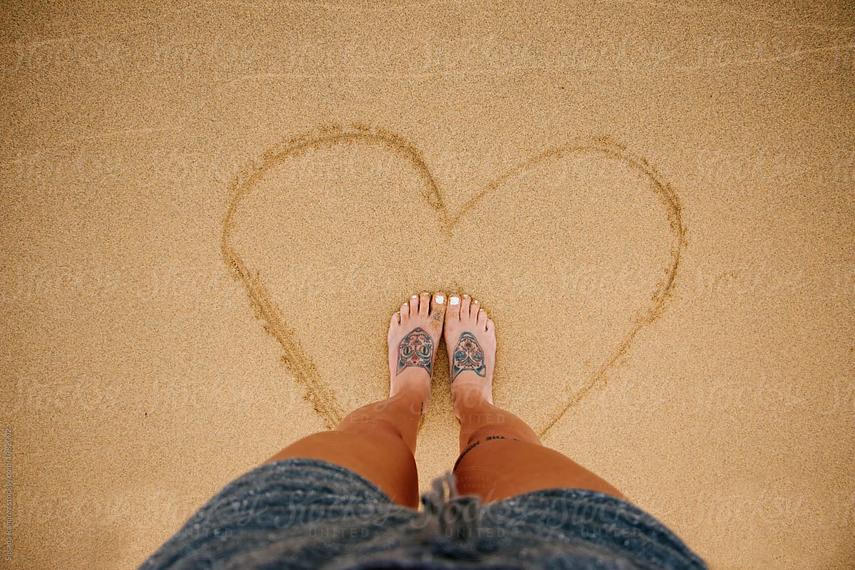 Feet woman inside a heart drawn in the sand
