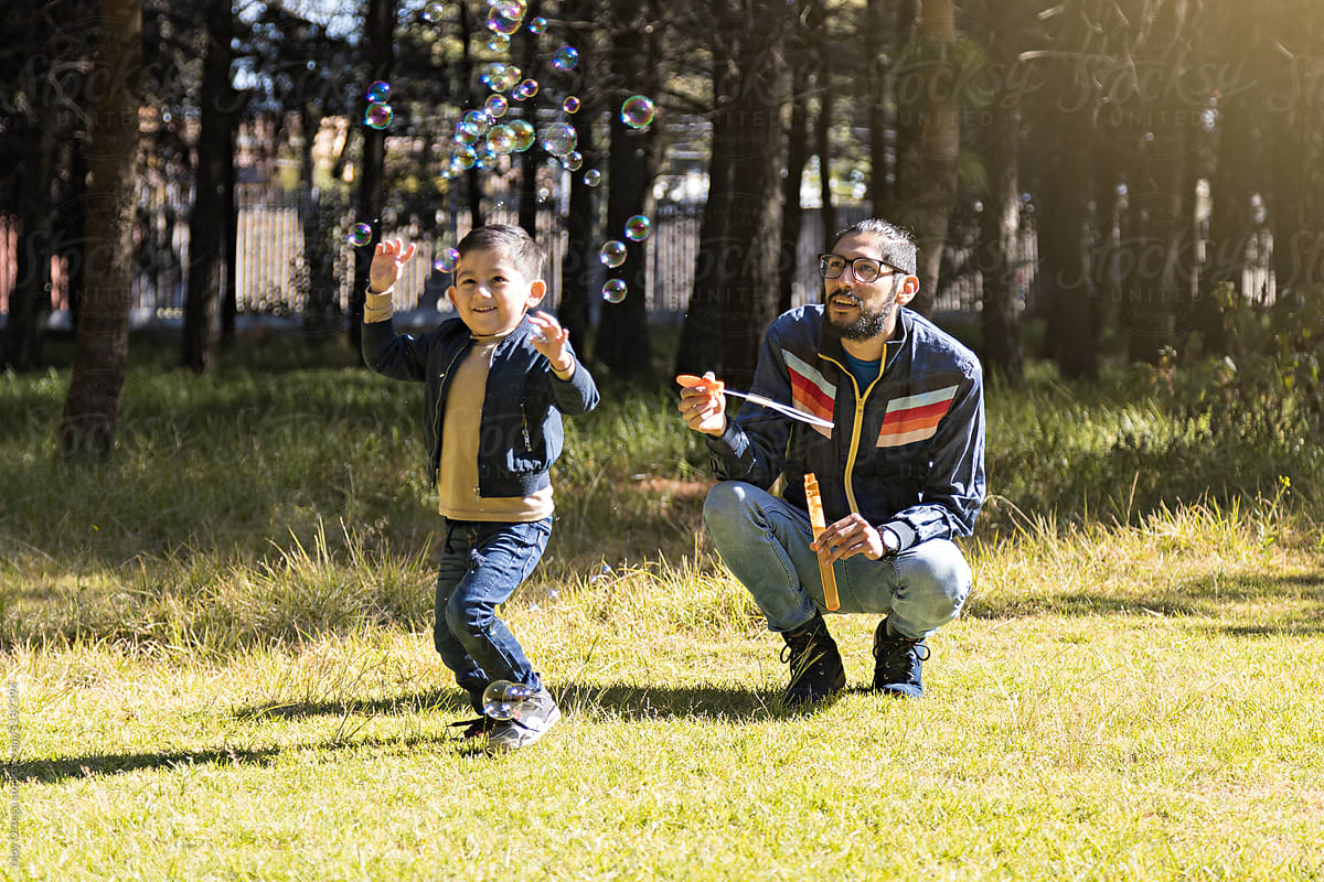 Father And Son Blowing Bubbles In A Park