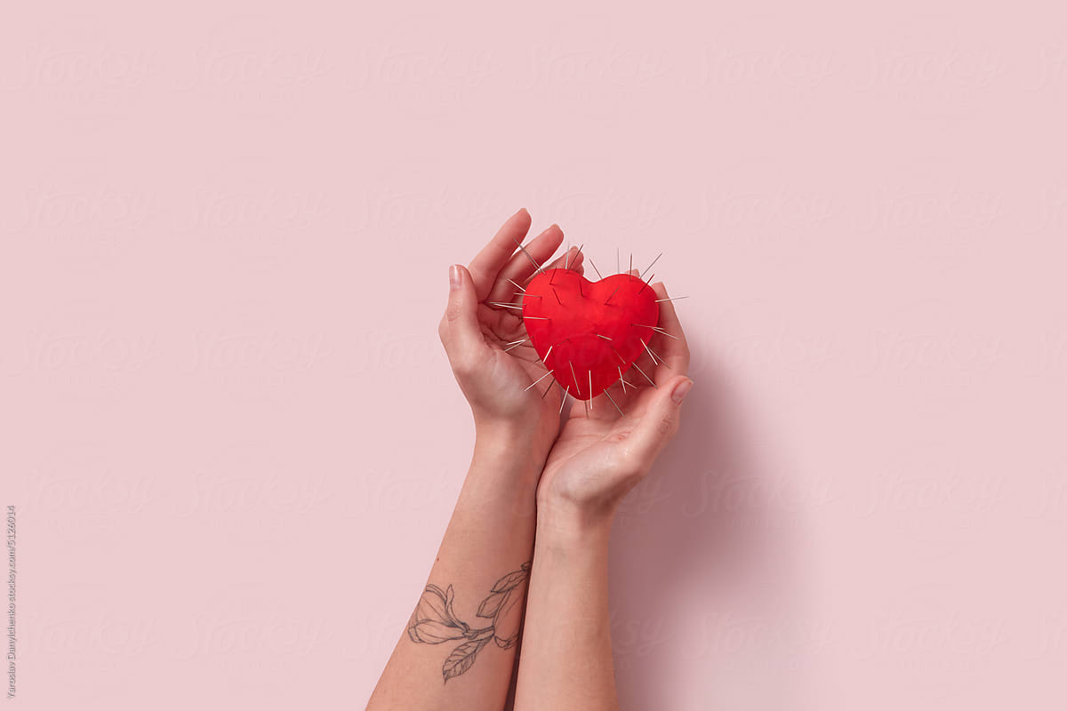 Red heart with thorns in tattooed woman\'s hands.